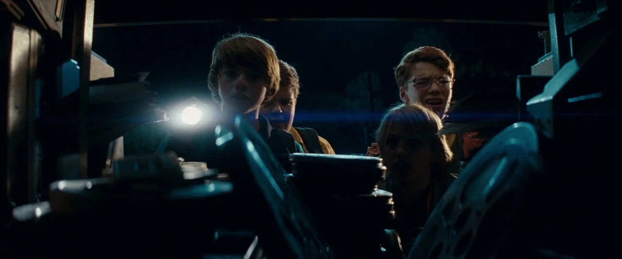 Super 8 (2011) movie still: medium — A dark indoor space filled with stacks of metal film canisters and paper documents. Four young boys stand…