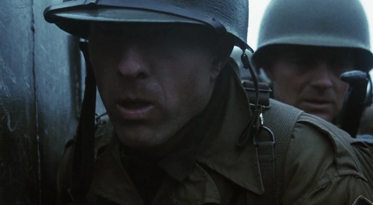 Saving Private Ryan (1998) movie still: medium — Two soldiers in full military gear huddle together inside a cramped, earth-walled trench. They…