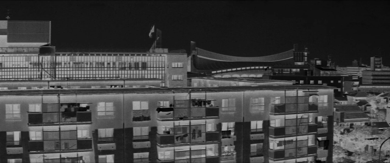 Branded To Kill (1967) movie still: establishing — A dense urban landscape at night features multi-story residential buildings with illuminated…