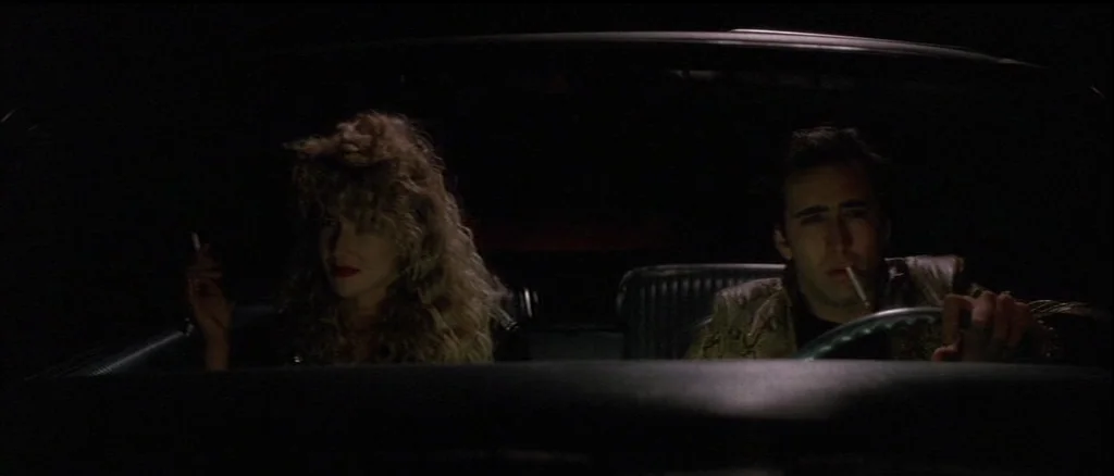 Wild At Heart (1990) movie still: medium — The interior of a car at night showing two people in the front seats. The man drives while the woman sits…