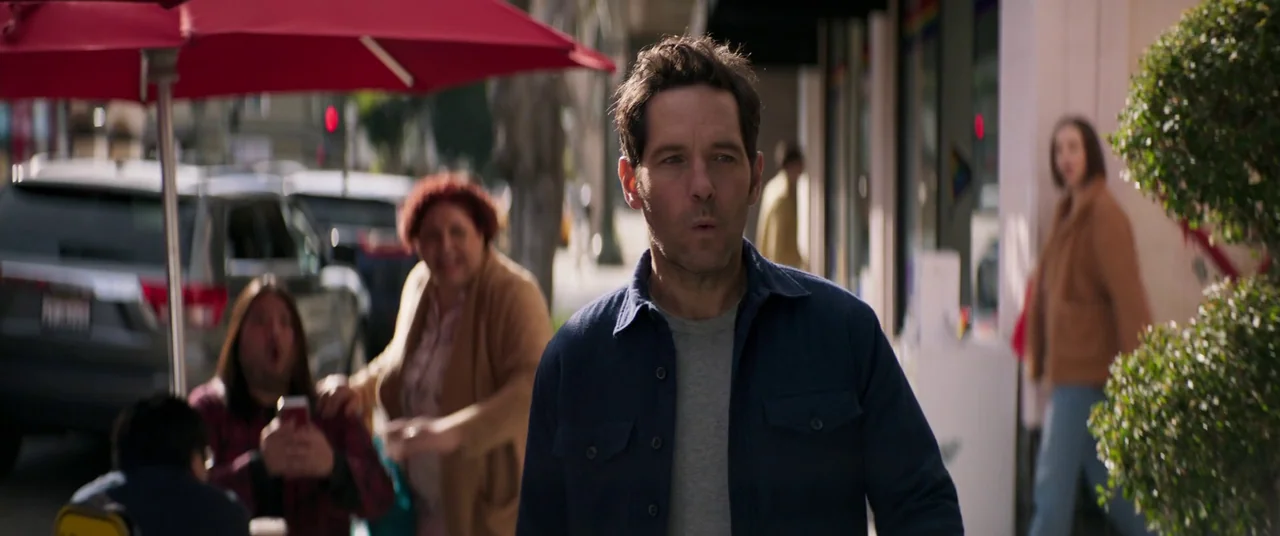 Ant-Man and the Wasp: Quantumania (2023) movie still: medium — A sidewalk with a red umbrella and storefronts in the background. A man walks forward…