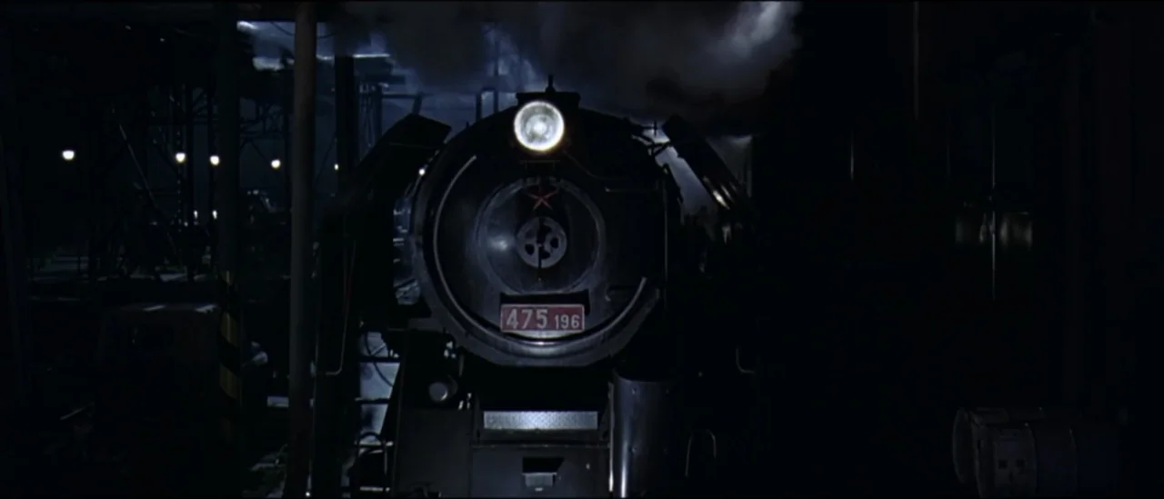 The Peacemaker (1997) movie still: medium — A large steam locomotive occupies the center of a dark train depot at night. Thick white steam billows…