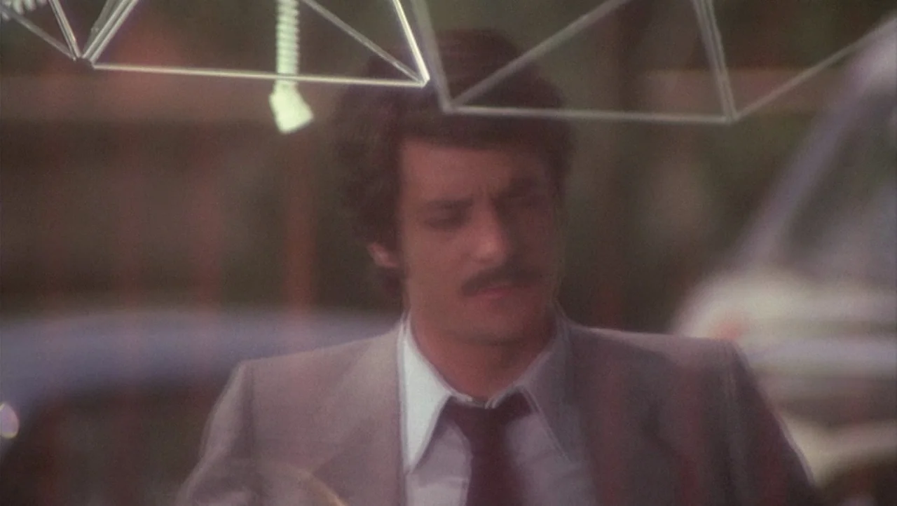 The Black Belly of the Tarantula (1971) movie still: medium — A man stands in an outdoor night setting near a structure with triangular geometric…