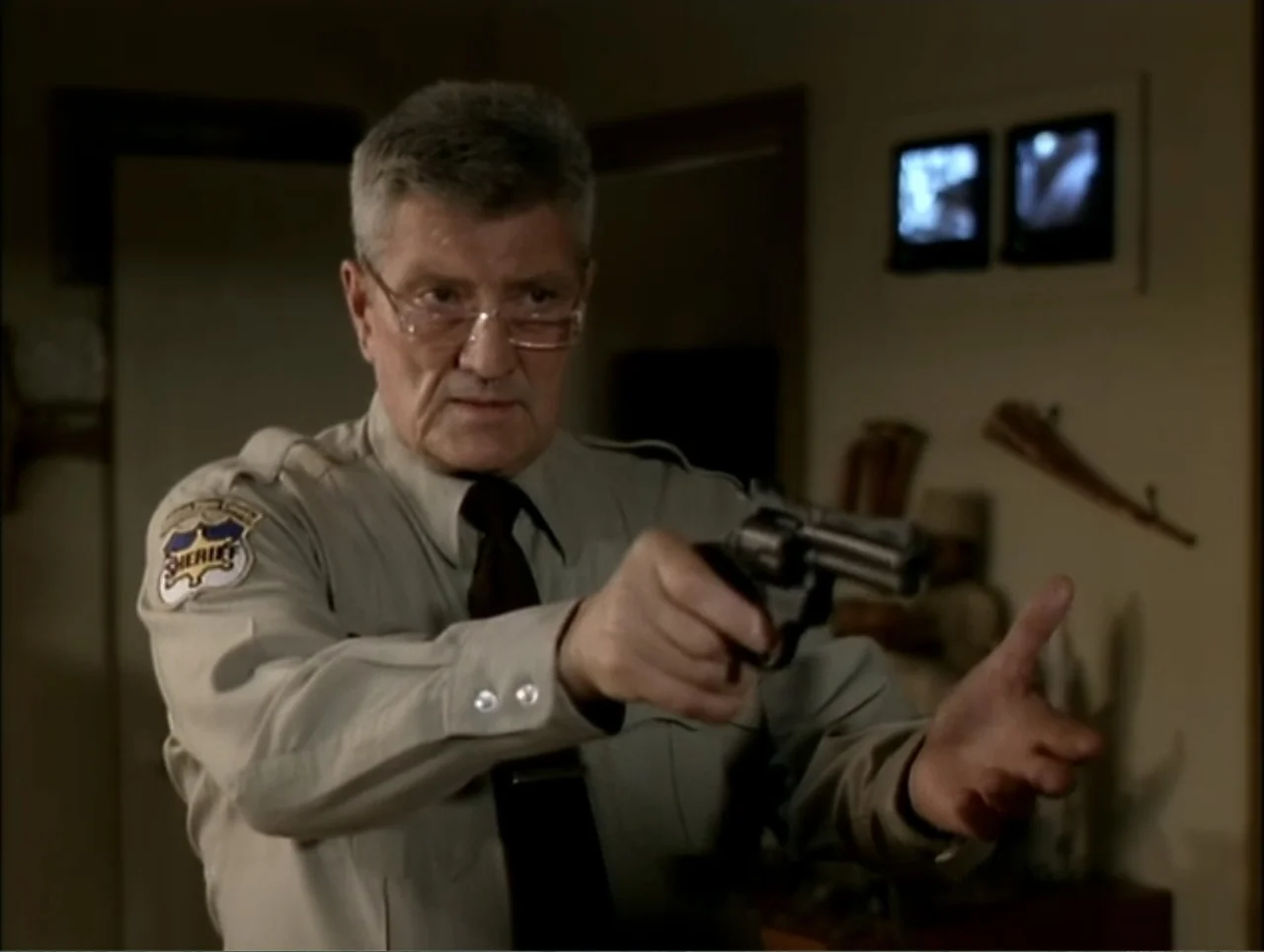 At the Midnight Hour (1995) movie still: medium — An indoor office space contains security monitors mounted on the wall. An older sheriff in a tan…