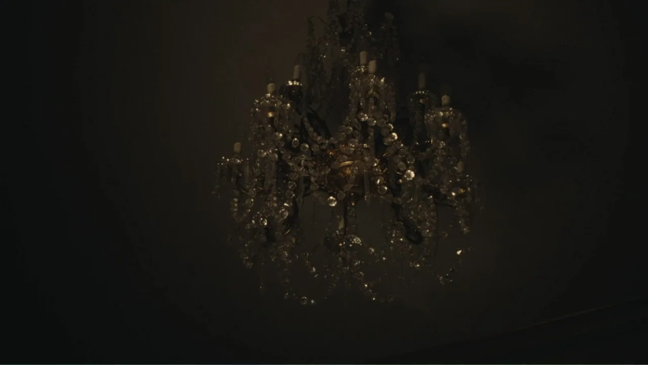 Demon in the White House (2021) movie still: establishing — A dark, ornate interior space features an elaborate crystal chandelier hanging from the…