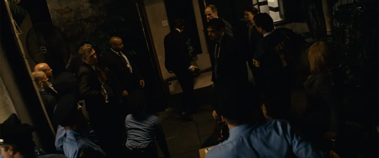 Now You See Me (2013) movie still: medium — A dimly lit narrow corridor contains multiple police officers and FBI agents. The group stands together…