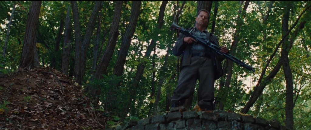 Inglourious Basterds (2009) movie still: fullbody — A dense woodland with mature trees and a dirt mound in the foreground. A man wearing military…