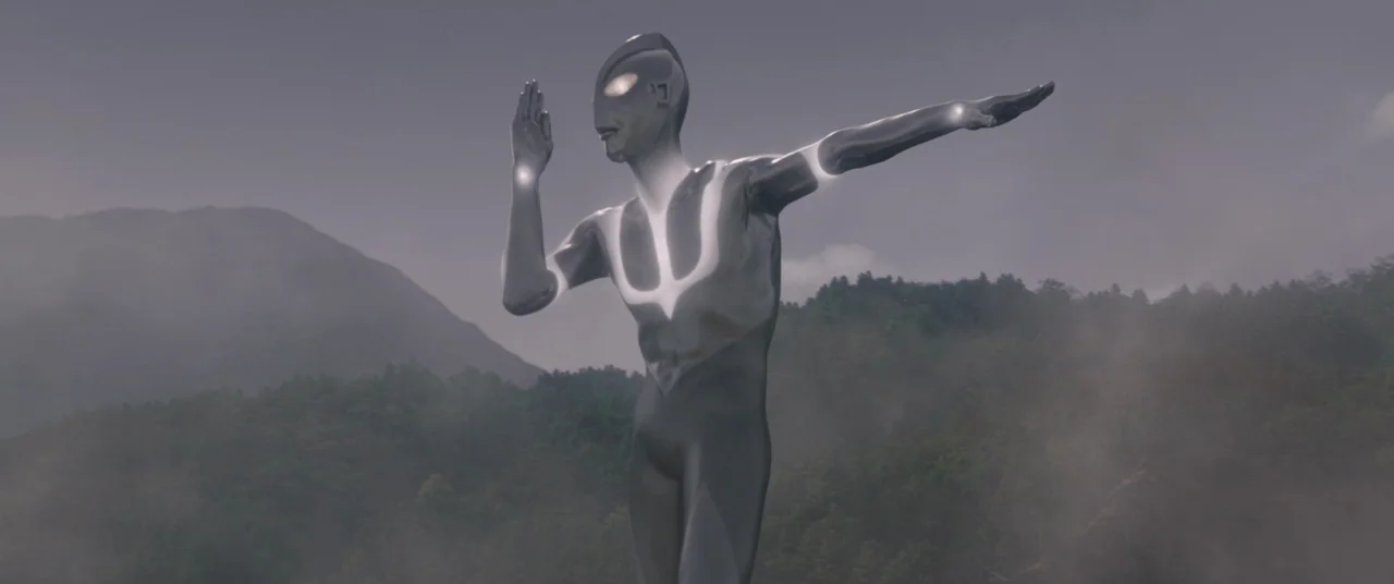Shin Ultraman (2022) movie still: fullbody — A towering metallic figure stands in a misty mountain landscape during the day. The humanoid being…