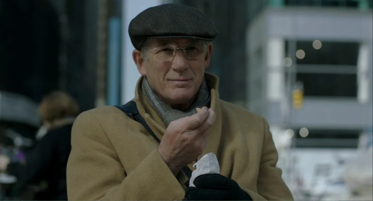Norman: The Moderate Rise and Tragic Fall of a New York Fixer (2016) movie still: medium — A man in a tan overcoat stands on a busy urban sidewalk.…