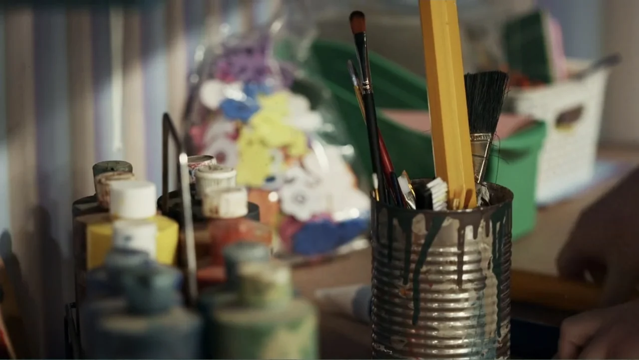 Mr. Dressup: The Magic of Make Believe (2023) movie still: closeup — An artist's workstation contains a metal tin overflowing with paintbrushes and…