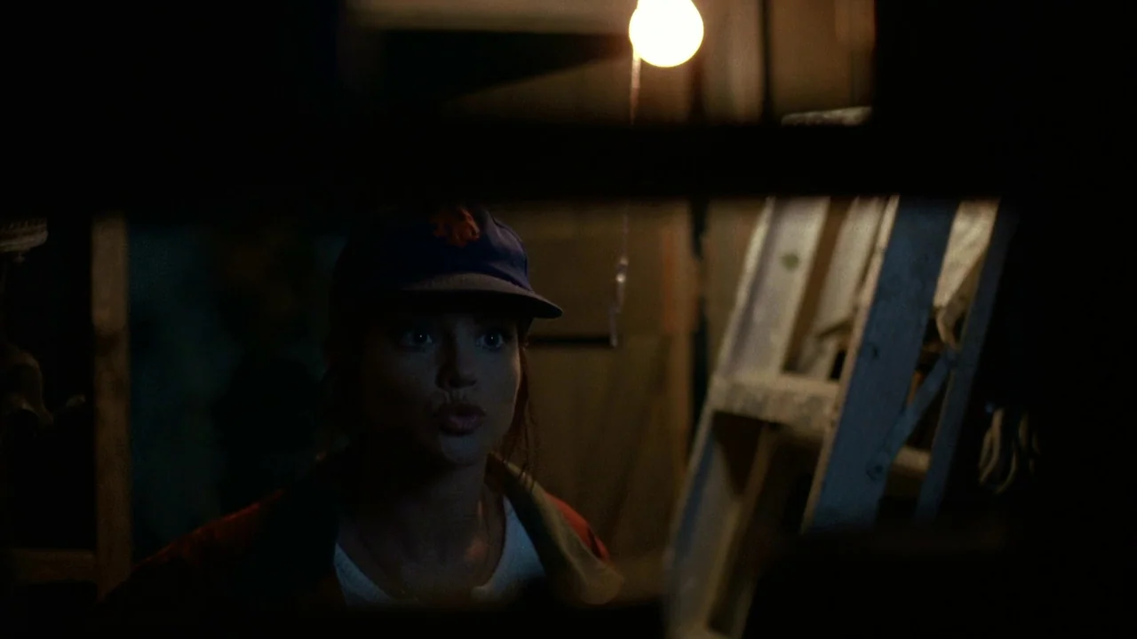Jason Goes To Hell (1993) movie still: medium — A cluttered, dark basement contains a wooden ladder leaning against a wall. A young woman wearing a…