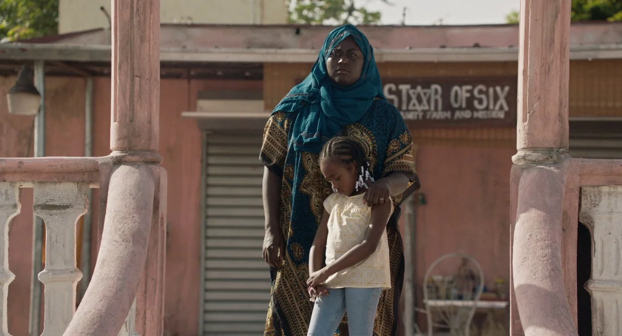 The Day Shall Come (2019) movie still: fullbody — A peach-colored building with a porch features a sign reading Star of Six. A woman wearing a hijab…