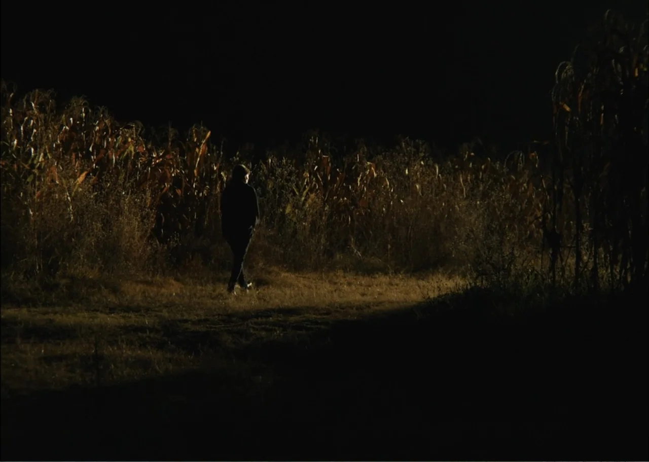 A Fisherman's Tale (1976) movie still: wide — A dark night landscape featuring a dense patch of dry corn stalks. A lone figure in dark clothing…