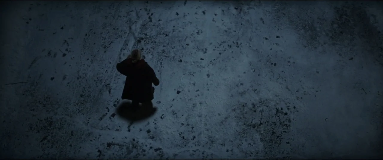 Vicious (2025) movie still: wide — A snow-covered area at night is lit from above. A lone figure in a coat stands in the center of the frame.