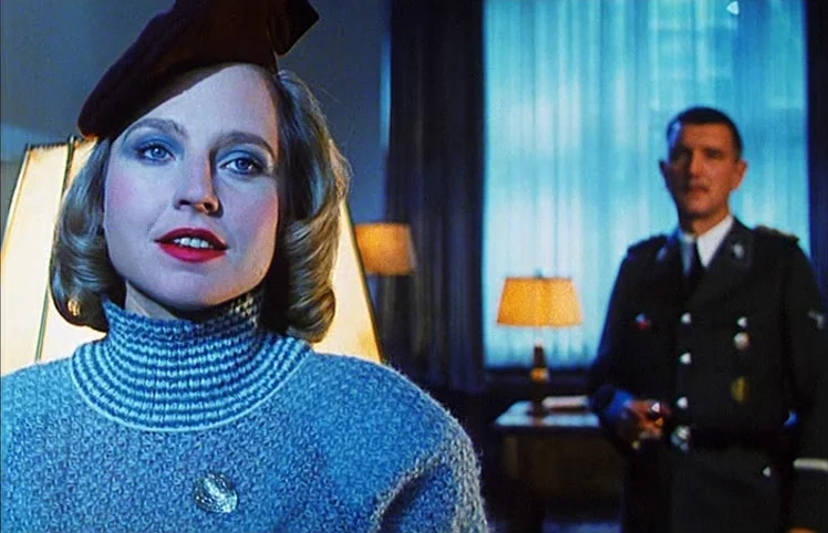 Lili Marleen (1981) movie still: medium — A dimly lit room features a window with blue light behind a formal military officer. In the foreground, a…