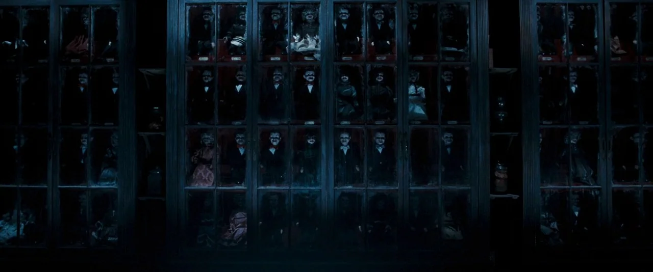 Dead Silence (2007) movie still: wide — Large wooden cabinets with glass panels are filled with numerous small dolls on shelves. Each cabinet…