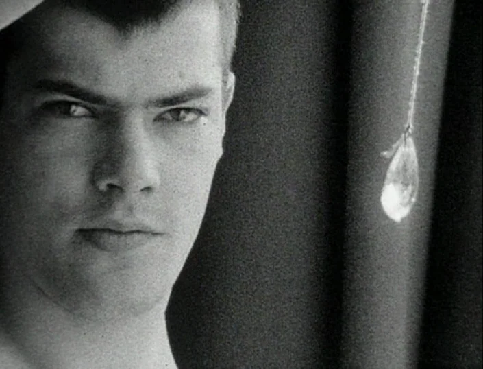 Glitterbug (1994) movie still: closeup — A man's face occupies most of the frame in a dark room. A small, glowing light-reflecting ornament hangs…