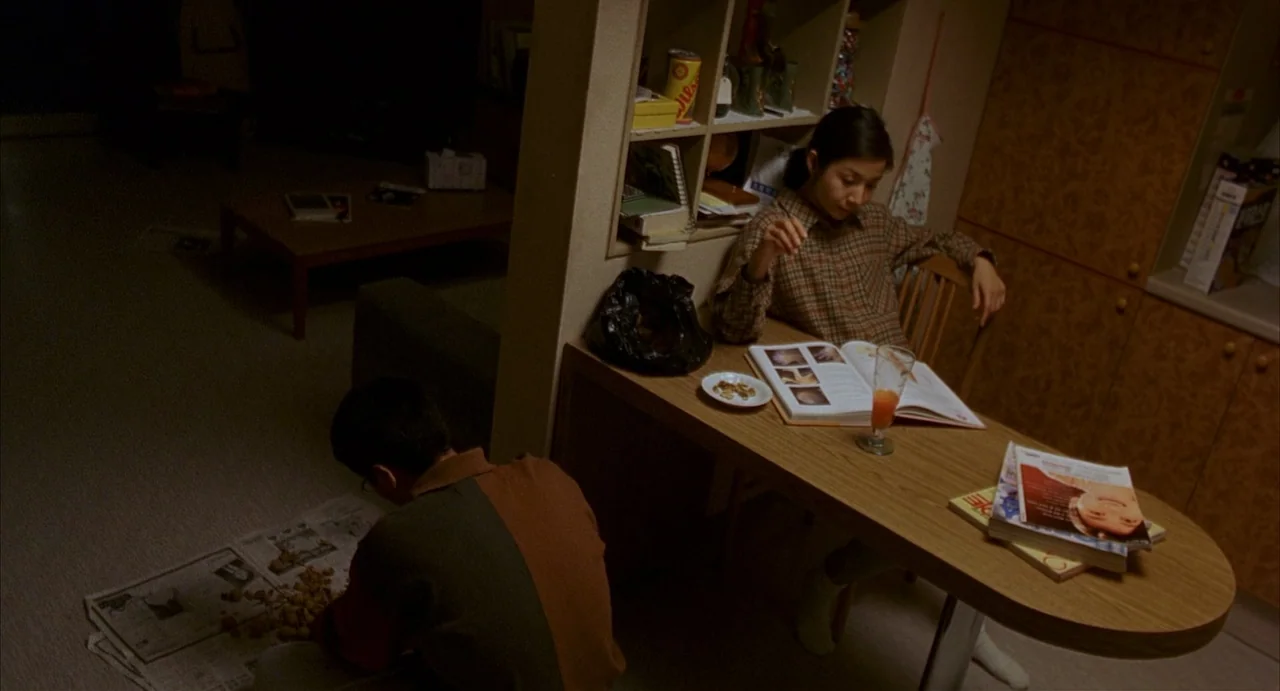 Barking Dogs Never Bite (2000) movie still: medium — An apartment interior features a dining table and floor space used for tasks. A man squats on…