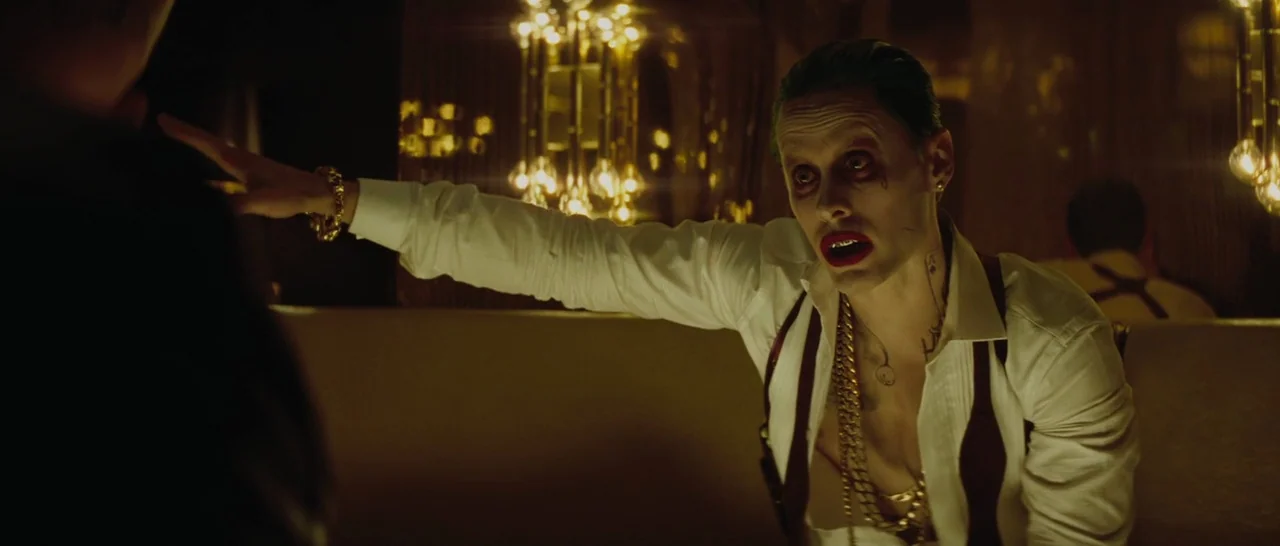 Suicide Squad (2016) movie still: medium — A dimly lit club booth features warm, decorative spherical light fixtures in the background. A man with…