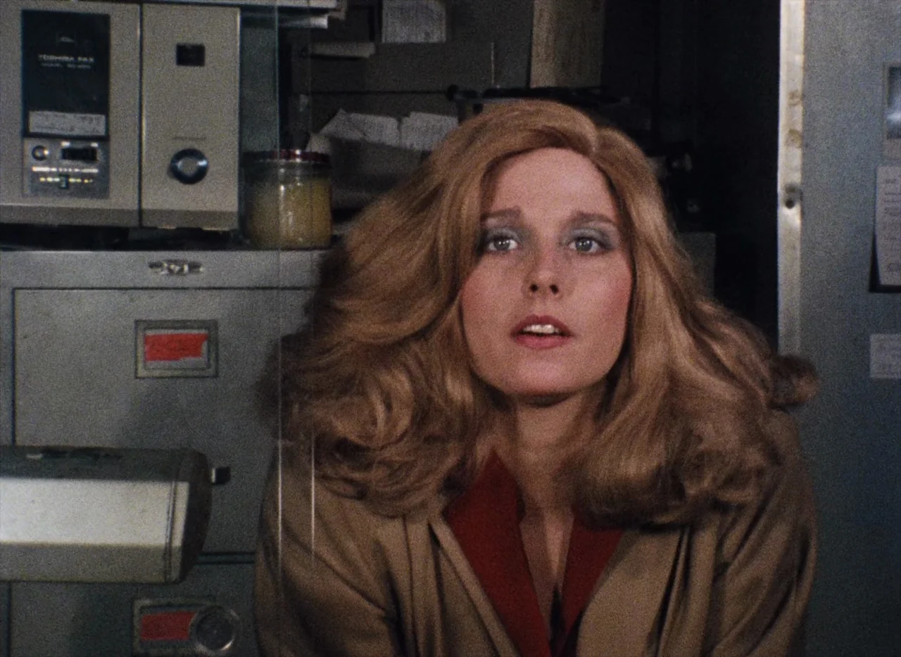 Basket Case (1982) movie still: closeup — An office environment with metal filing cabinets and vintage electronics visible behind the subject. A…