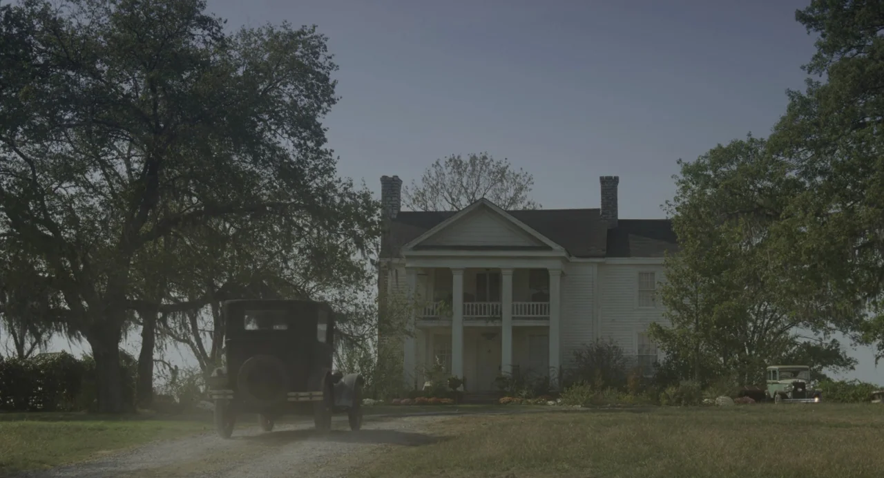 The Green Mile (1999) movie still: wide — A two-story white plantation-style house with tall columns sits behind a gravel drive. A vintage black car…