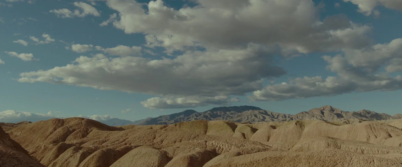 Last Days in the Desert (2015) movie still: establishing — A vast, barren desert landscape consists of rolling, sun-scorched tan hills. Cumulus…