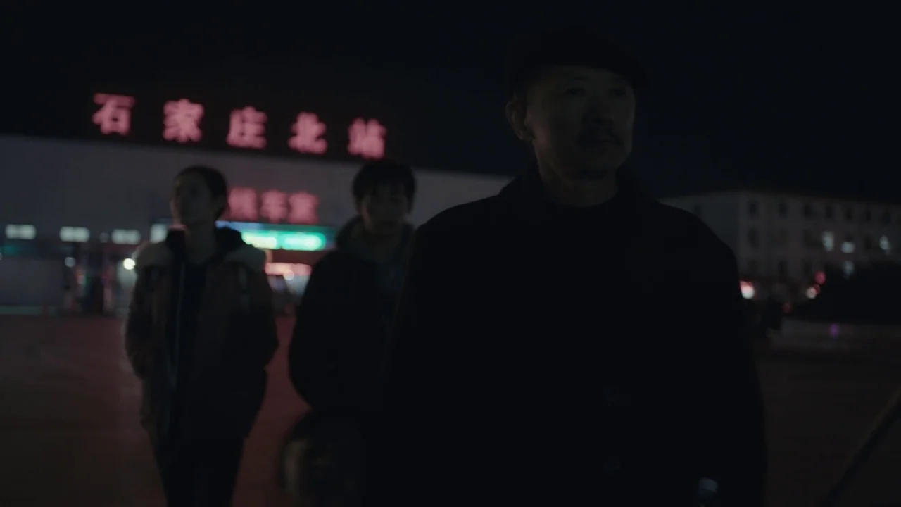 An Elephant Sitting Still (2018) movie still: medium — A dark, expansive concrete plaza outside a train station at night under dim light. Three…