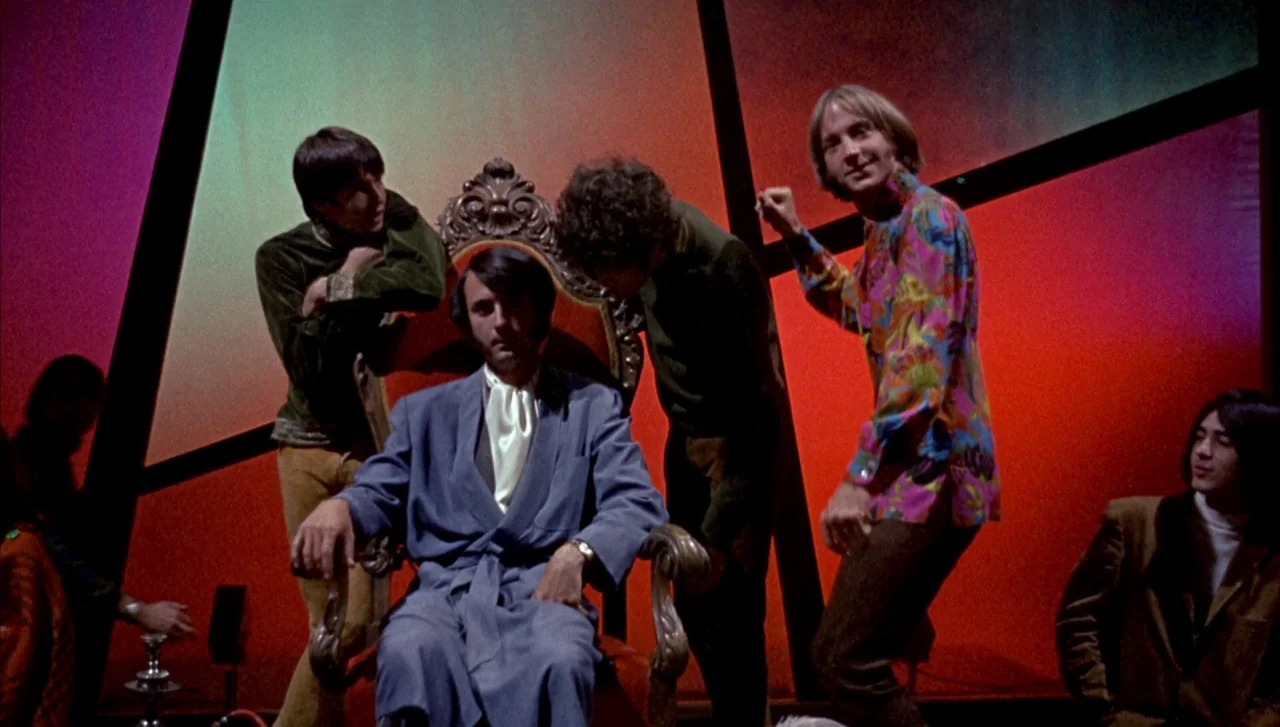 Head (1968) movie still: fullbody — A group of five men congregate around an ornate wooden throne in a colorful studio. The central man sits in a…