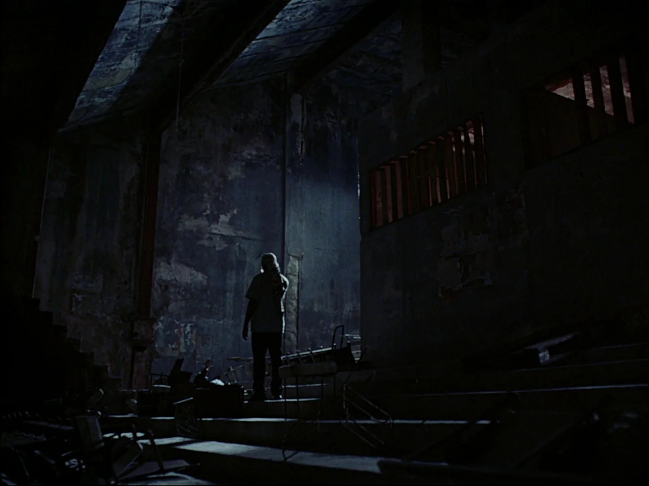 Guava Island (2019) movie still: wide — A dilapidated, shadowy auditorium features stacked concrete tiers and debris scattered across the floor. A…