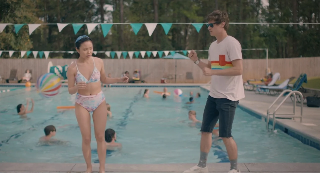 The Map of Tiny Perfect Things (2021) movie still: fullbody — A public outdoor swimming pool surrounded by a wooden fence and turquoise bunting. A…