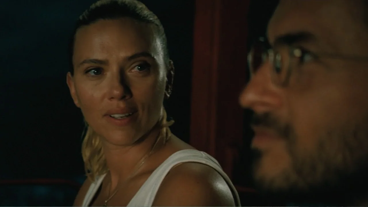 Jurassic World Rebirth (2025) movie still: medium — A dimly lit enclosed passenger car provides the background for this conversation. A woman looks…