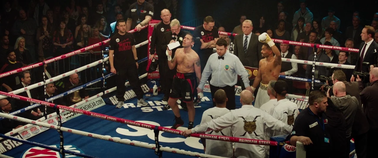 Journeyman (2017) movie still: wide — A high-angle view of a boxing ring containing two fighters and a referee. The scene shows the moments after a…