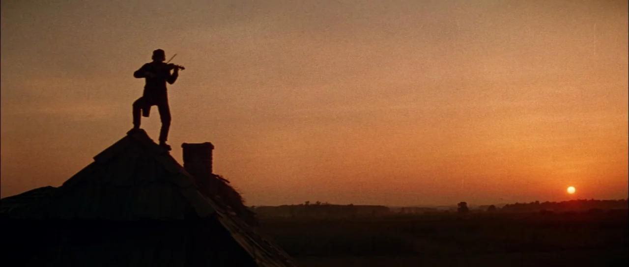 Fiddler On The Roof (1971) movie still: wide — A rural landscape at sunset under a vast, clear, warm-toned sky. A man stands on the sloped ridge of…