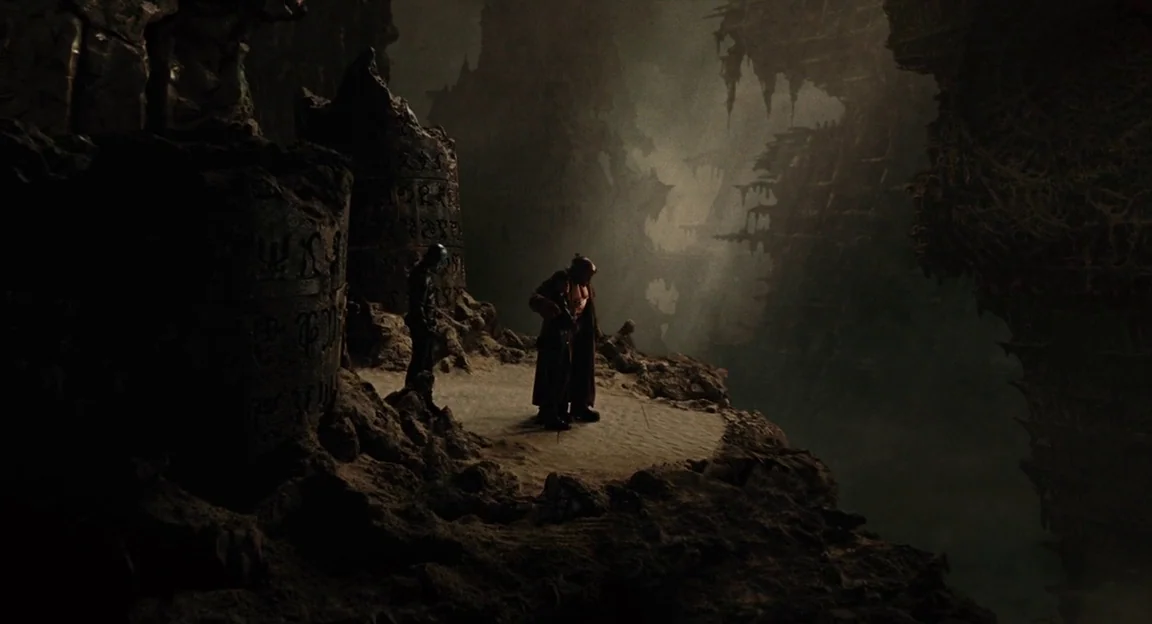 Hellboy II: The Golden Army (2008) movie still: wide — A dark, jagged cavern contains massive carved pillars and a deep, shadowy chasm floor. Two…