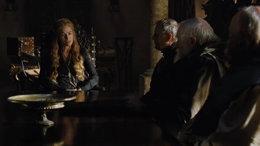 Game of Thrones (2015) movie still: medium — A stone council chamber features a long wooden table with a metallic bowl centerpiece. A blonde woman…
