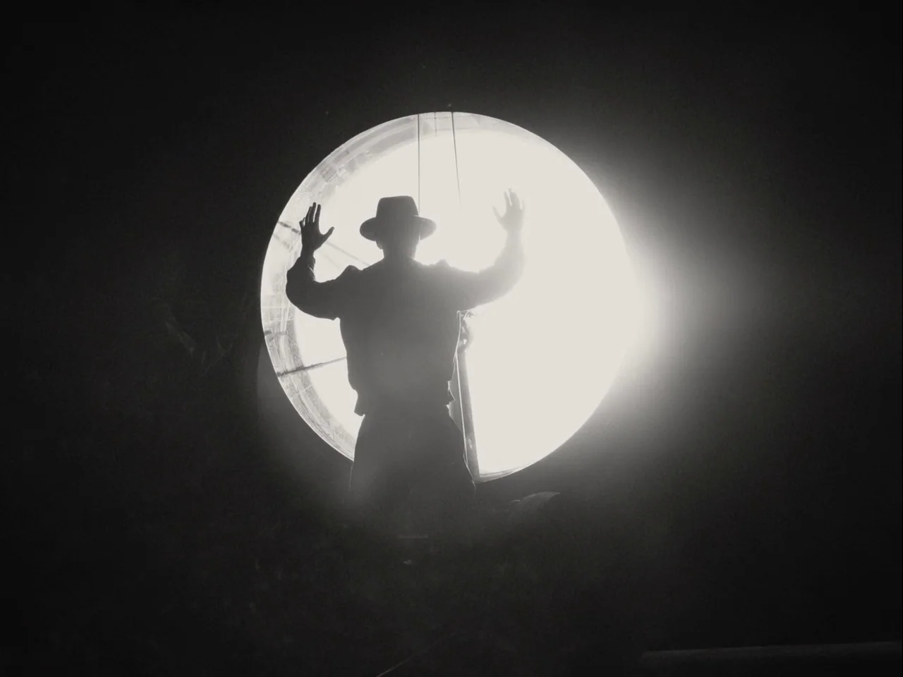 Blonde (2022) movie still: medium — An industrial setting at night features a large circular light source. A man stands in front of the light with…