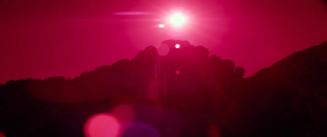 Seneca: On The Creation Of Earthquakes (2023) movie still: establishing — A jagged, silhouetted mountain range stands against a bright, uniform red…