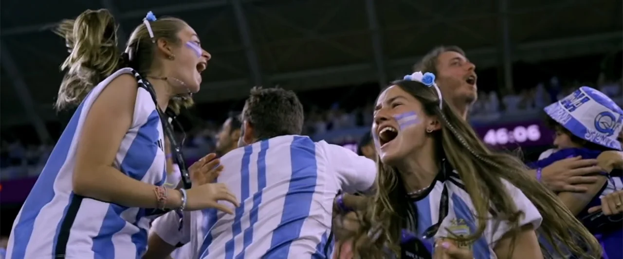 I Choose to Believe (2023) movie still: medium — A crowded stadium section at night is filled with spectators in team colors. Two young women are…