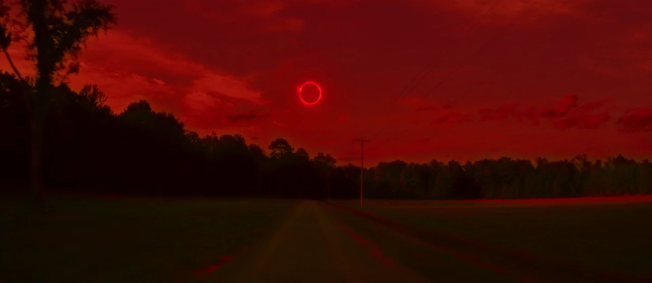 Gerald’s Game (2017) movie still: establishing — A dark rural dirt road runs through a landscape of silhouetted trees at dusk. A total solar eclipse…