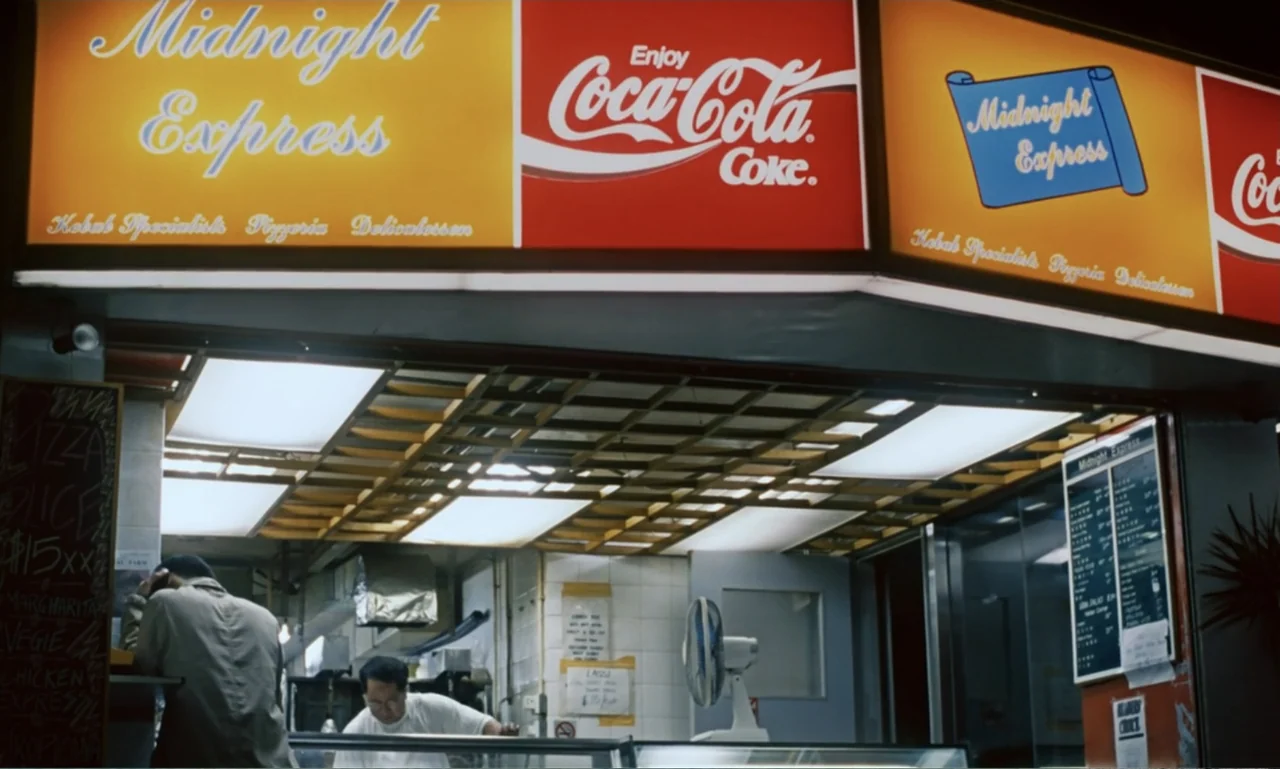 Chungking Express (1994) movie still: medium — A late-night eatery features bright yellow and red signage for a business named Midnight Express. A…