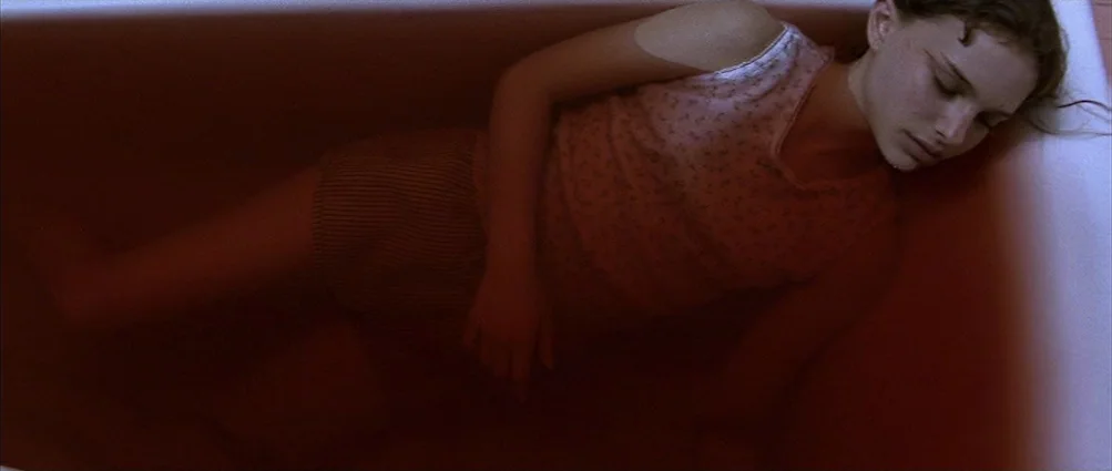 Heat (1995) movie still: medium — A porcelain interior filled with reddish water tinted by a substance. A young woman lies in the water with her…