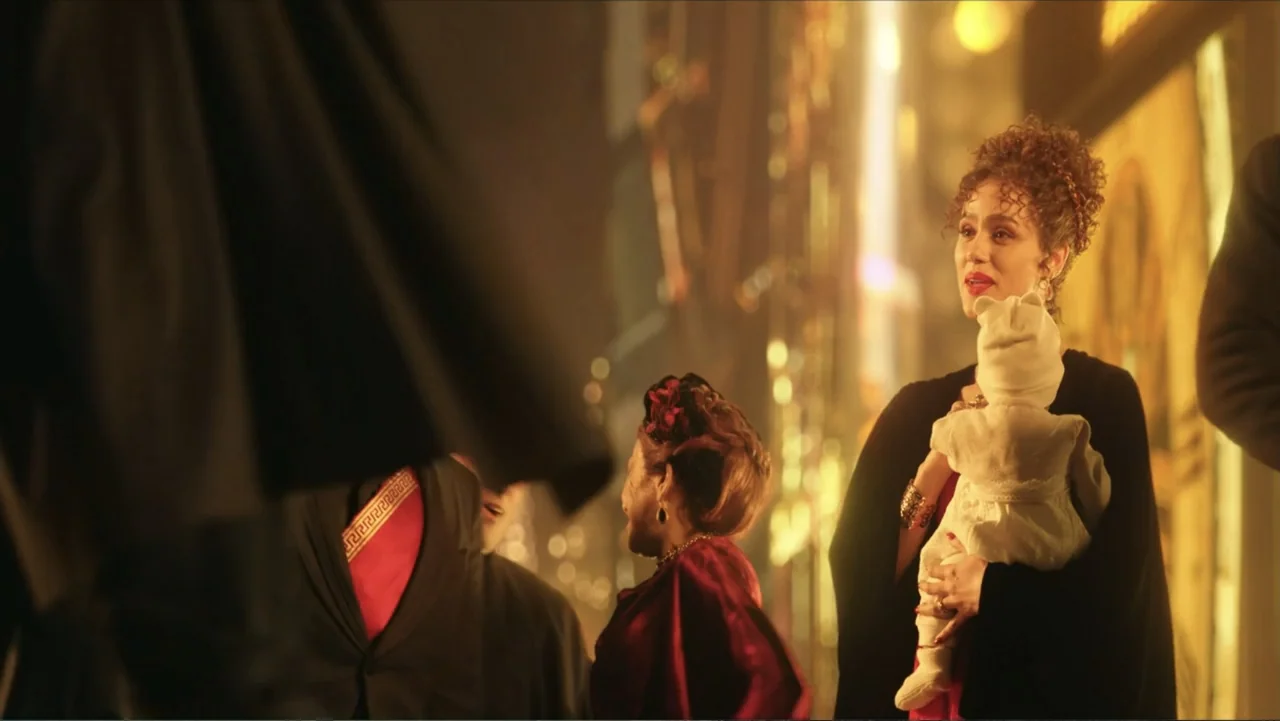 Megalopolis (2024) movie still: medium — A blurred city street at night with bright golden neon light in the background. A woman holds an infant…
