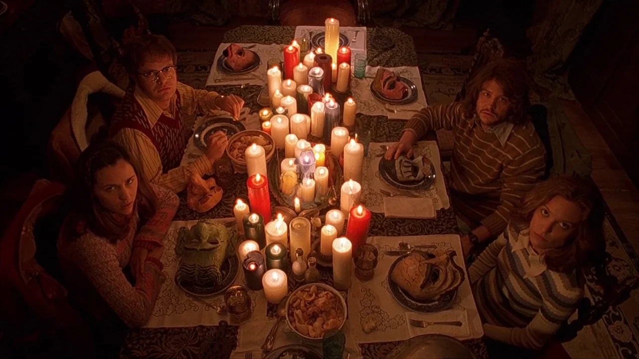 House of 1000 Corpses (2003) movie still: wide — A formal dining table is crowded with dozens of burning candles and decorative masks. Four…