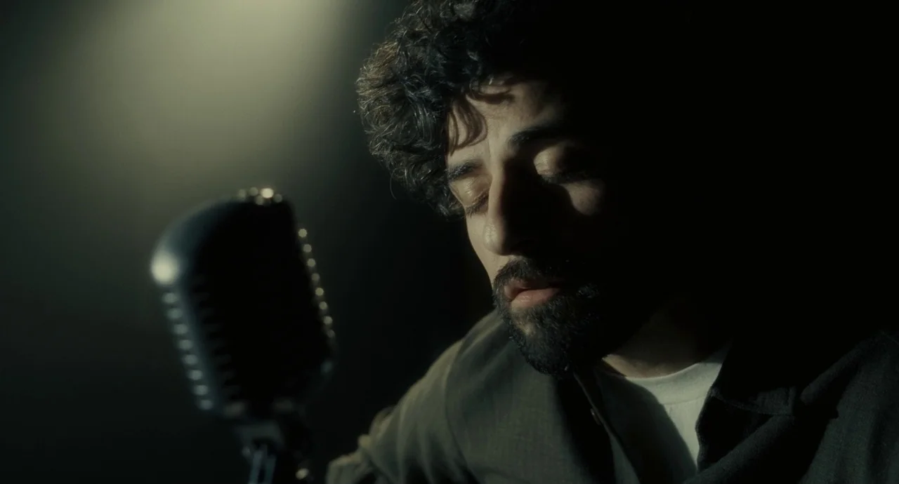 Inside Llewyn Davis (2013) movie still: closeup — A dark, minimally lit recording booth contains only a microphone and a musician. The man sings…