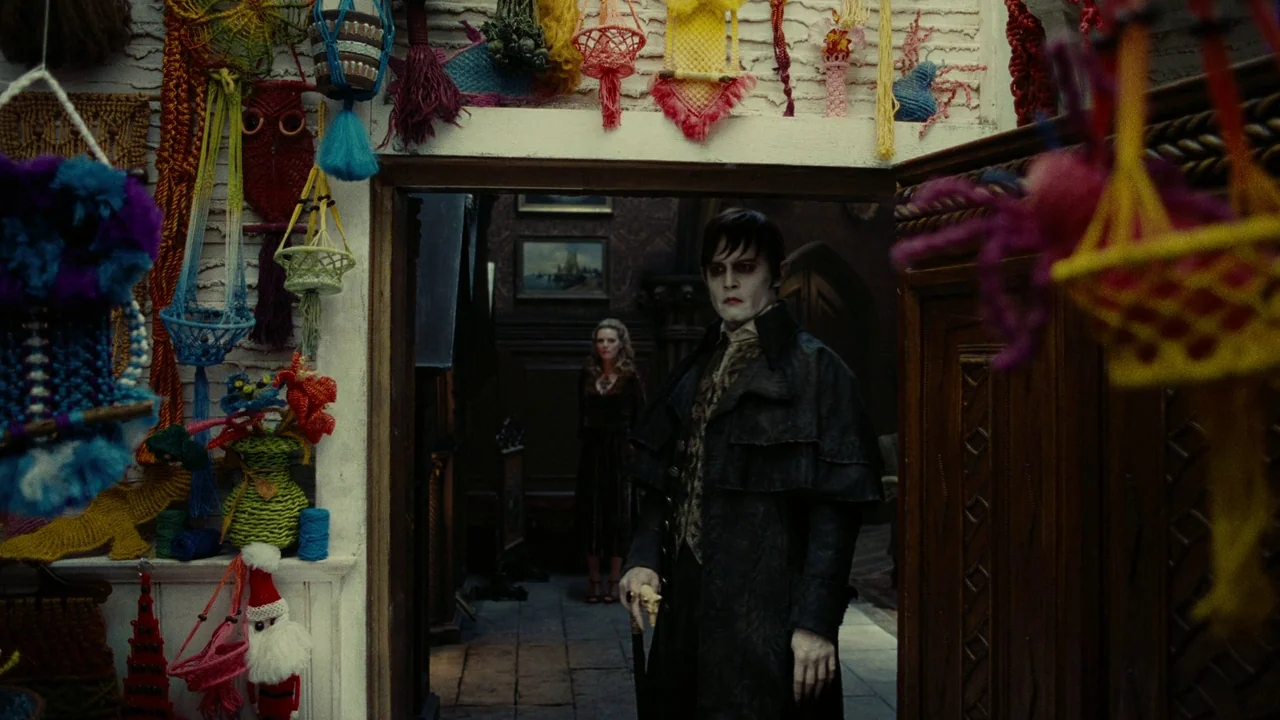 Dark Shadows (2012) movie still: medium — A craft shop interior is densely packed with hanging colorful yarn macrame wall hangings. A pale man in a…