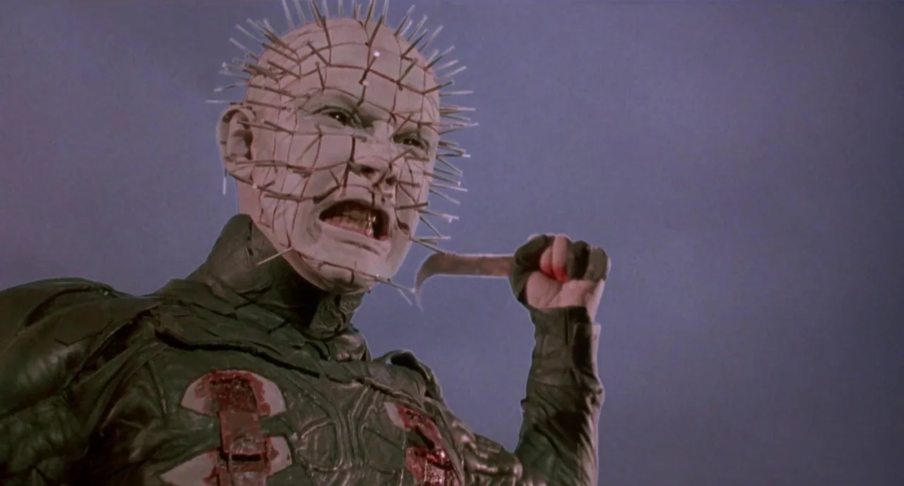Hellraiser III: Hell on Earth movie still: medium — A pale, pin-covered humanoid figure stands against a plain, flat, purplish-grey background. The…