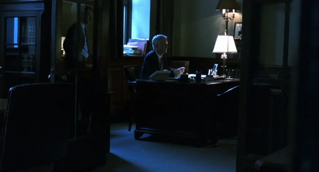 Traffic (2000) movie still: wide — A dark wood office features floor-to-ceiling shelving and a large leather desk. One man sits at the desk while a…