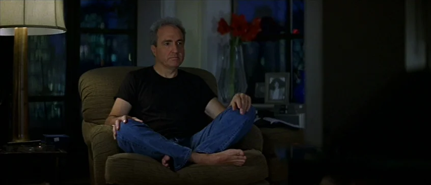 Man On The Moon (1999) movie still: medium — A dimly lit room with a man sitting in an armchair at night. The man watches television while red…