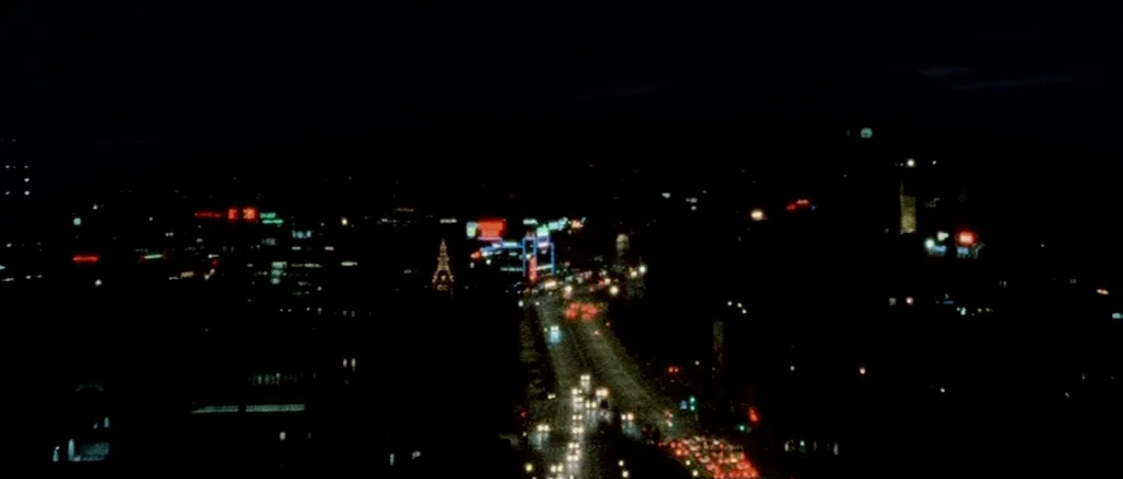 Reconstruction (2003) movie still: establishing — A sprawling nocturnal city vista viewed from an elevated perspective. Scattered glowing traffic…