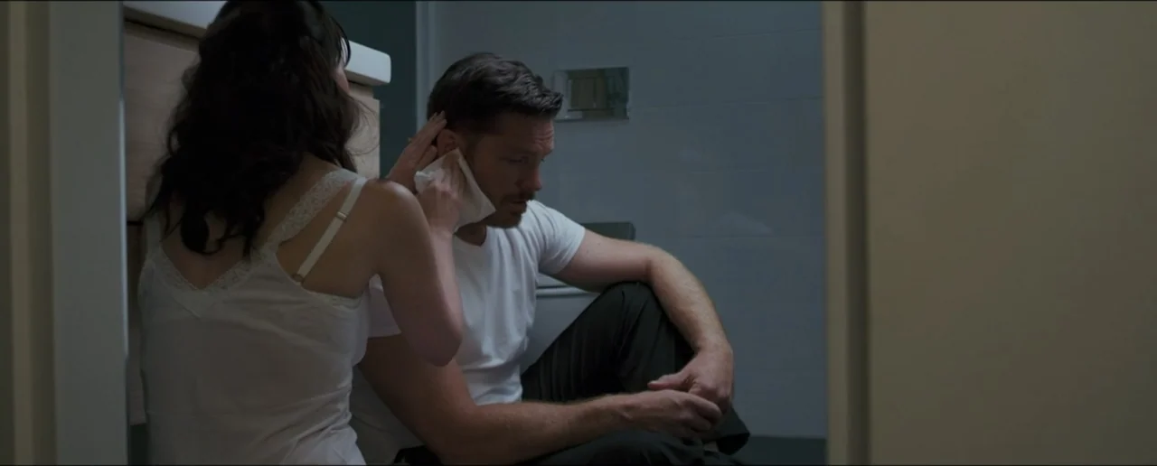 Hostages (2017) movie still: medium — A modern tiled bathroom provides the setting for the two individuals in the frame. A woman holds a tissue to a…